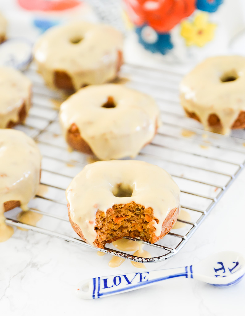 Carrot cake donuts with icing on a wire rack with a measuring spoon beside it.
