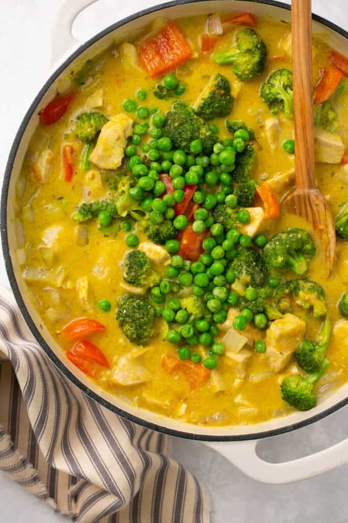 A large pan with chicken mango curry with frozen peas in it.