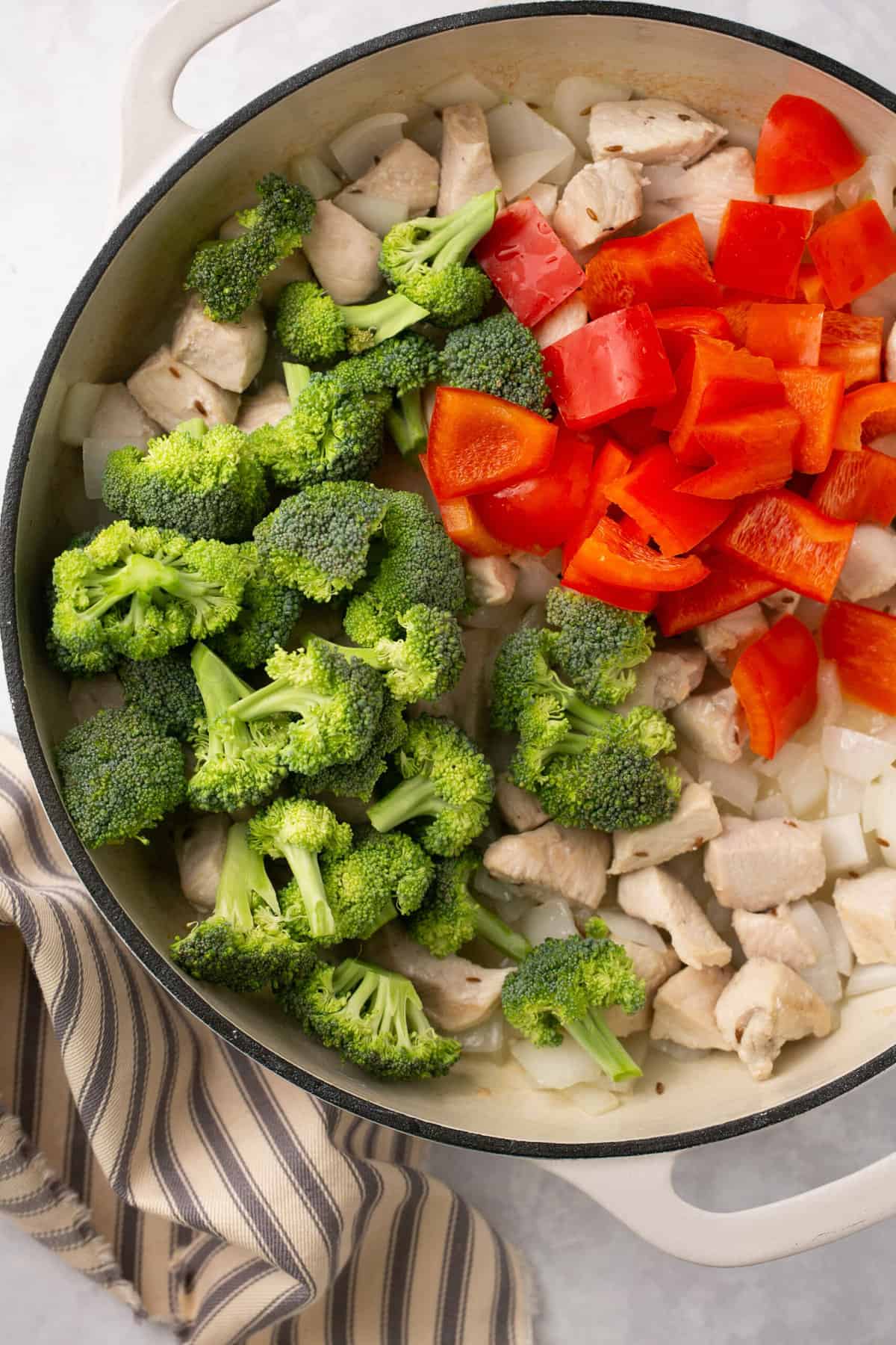 A pan with cooked chicken pieces, chopped broccoli and chopped red pepper in it.
