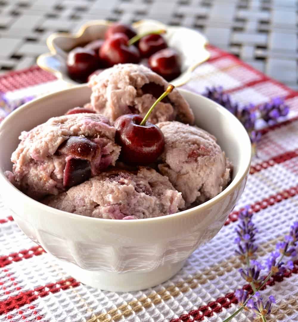 A bowl of lavender infused cherry ice cream topped with a fresh cherry. 