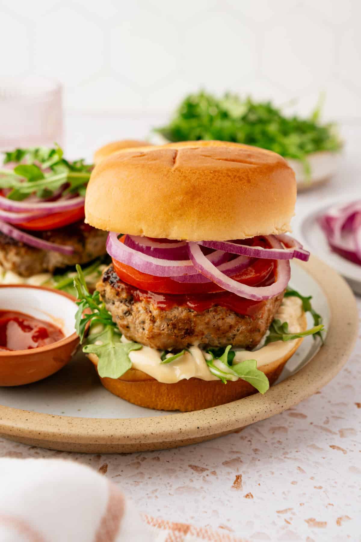 A burger in a bun topped with ketchup, mayonnaise, chopped tomatoes, onions and lettuce.