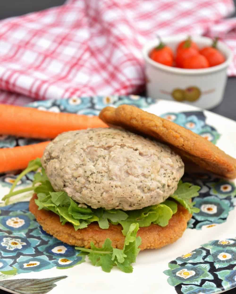 A pork burger in a bun with lettuce and carrots on the plate with it.