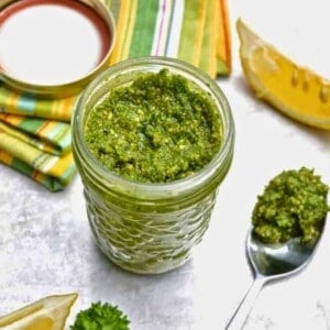 A glass jar filled with a green pesto sauce with a lemon wedge next to the jar.