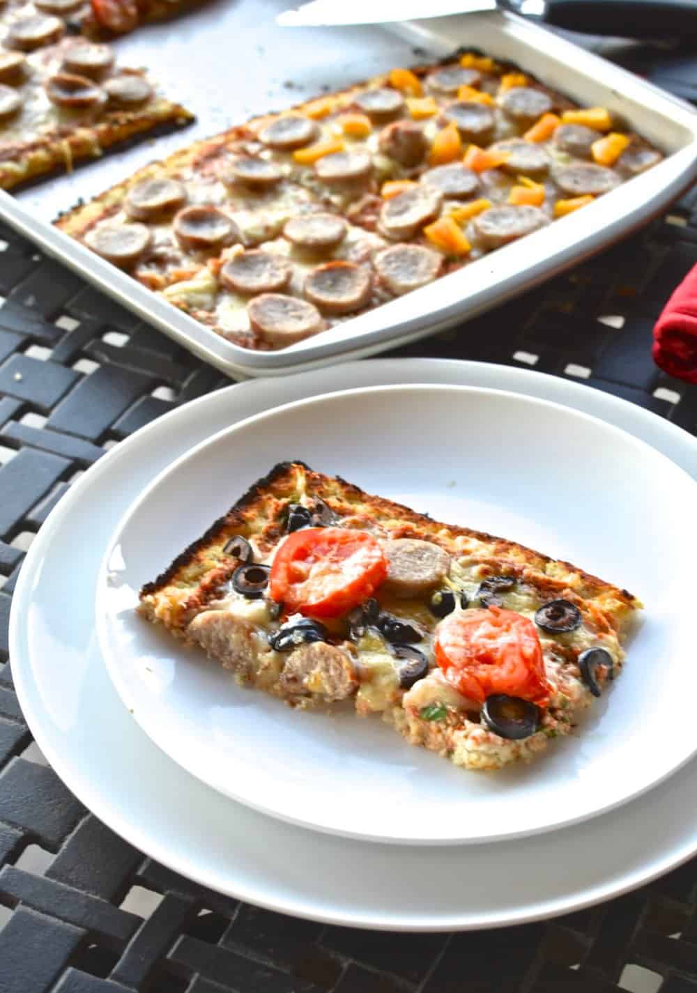 A pizza made with cauliflower crust on a plate topped with tomatoes and olives. 