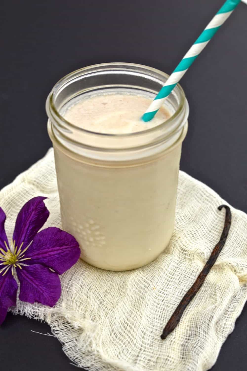 A large jar filled with a dairy free vanilla protein shake with a straw in it.