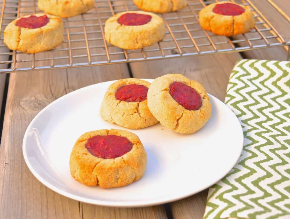 A white plate with three raspberry thumbprint cookies on it.