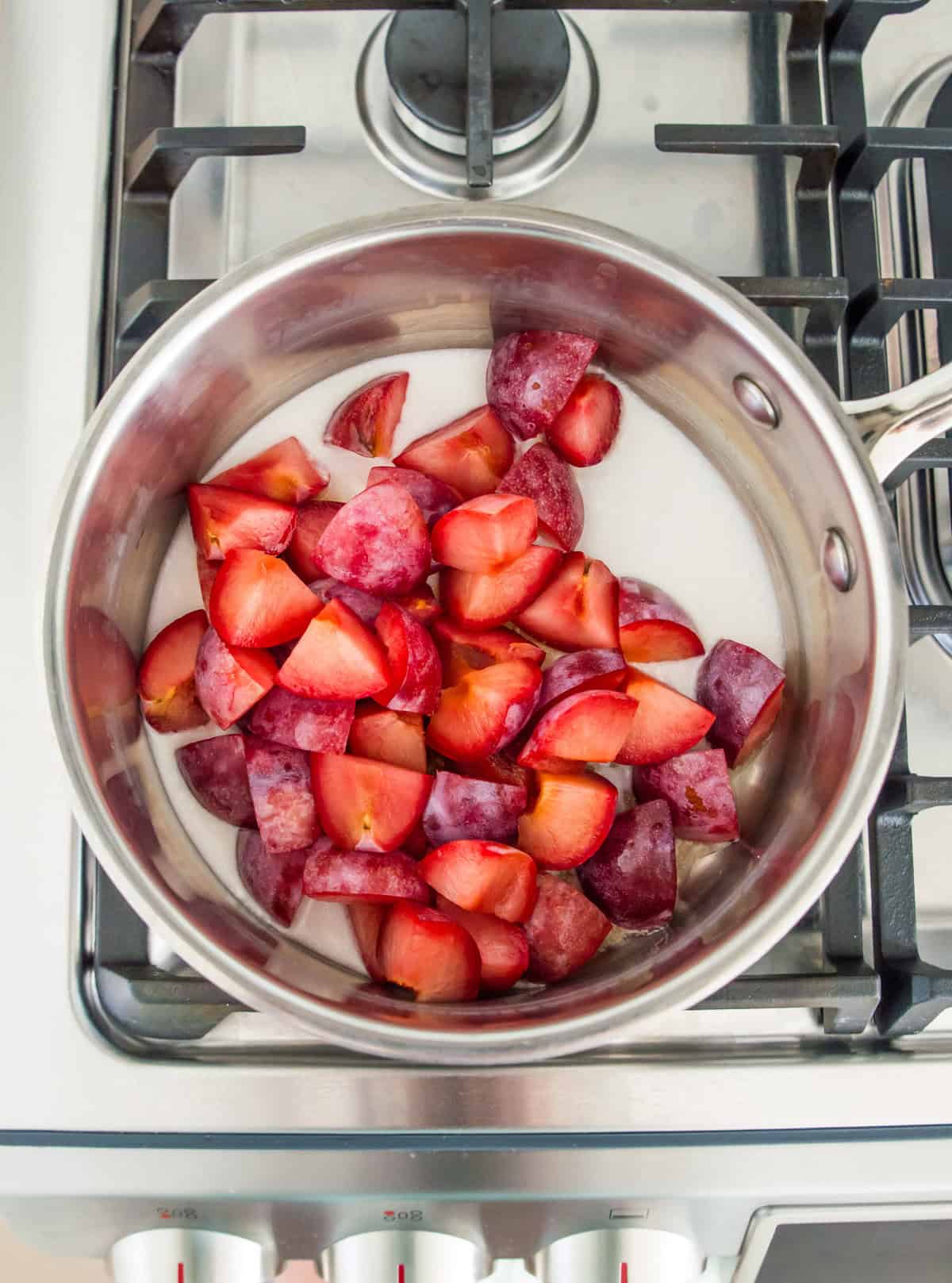 A pot on the stovetop with chopped plums and coconut milk in it.