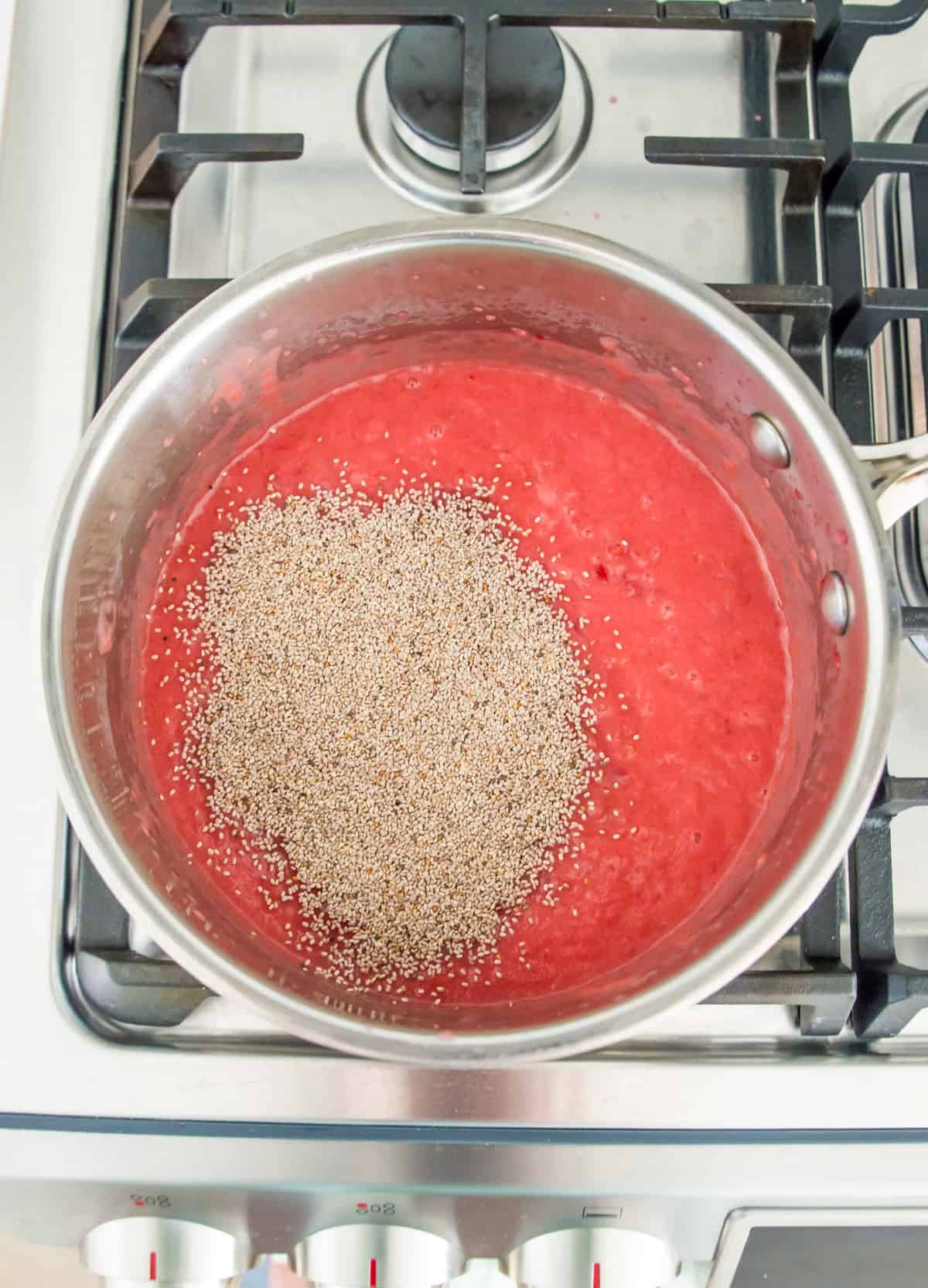 A pot on the stovetop filled with pureed plums and chia seeds over top of them. 