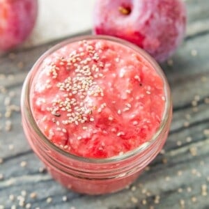 A jar of plum chia jam topped with chia seeds and two plums beside the jar.