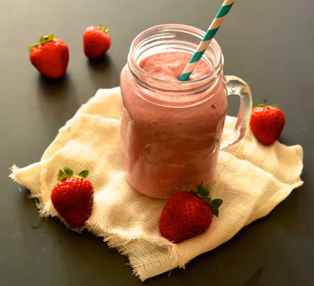 A glass filled with a vegan strawberry milkshake with a straw in it.
