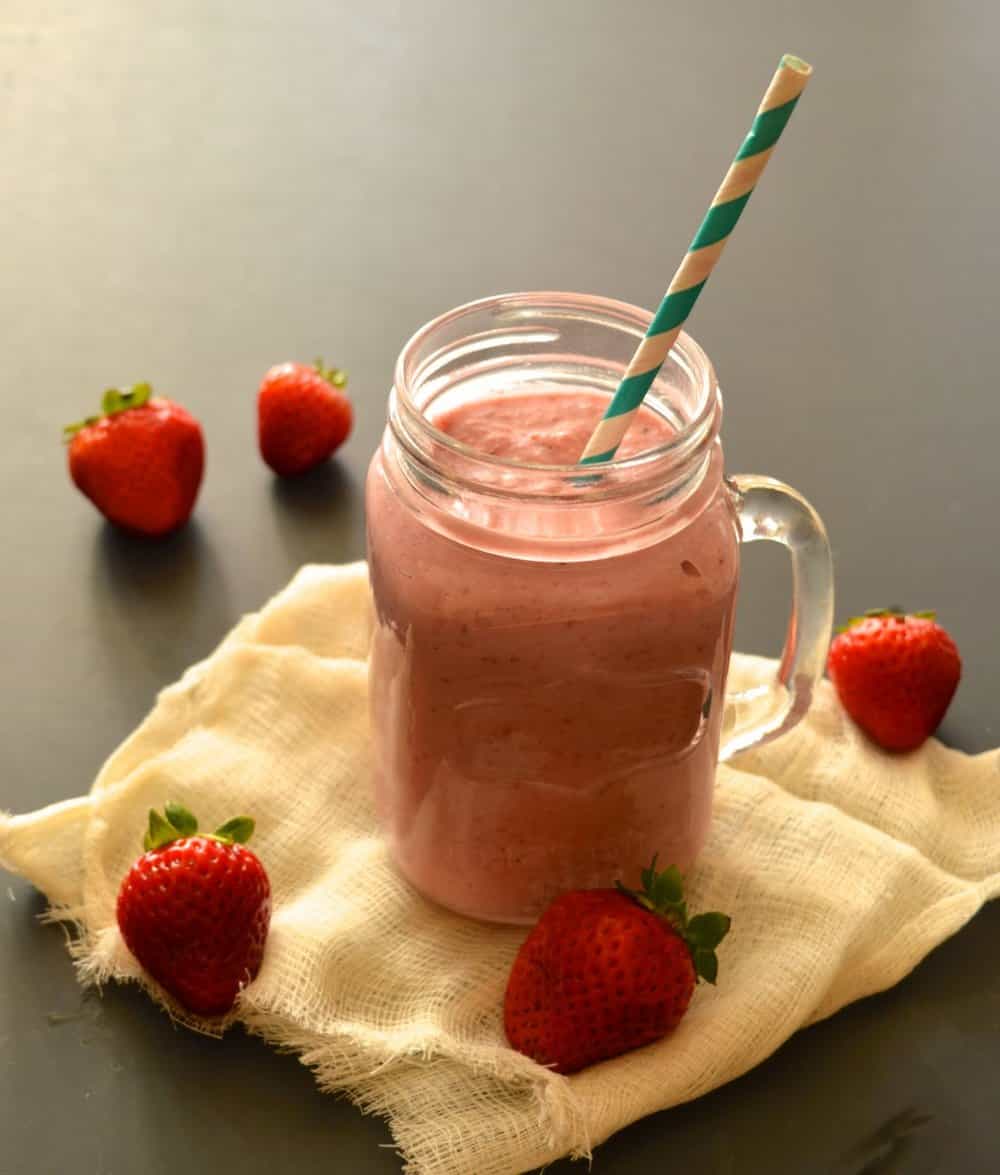 A glass full of a strawberry milkshake with a straw in it. 