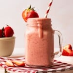 A glass filled with a strawberry milkshake with a straw in it.