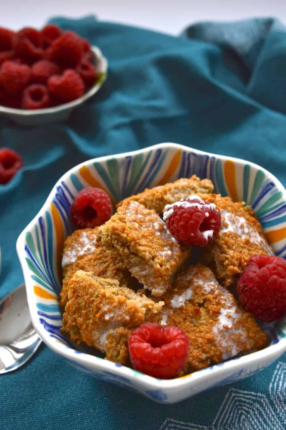A bowl of coconut cinnamon cereal topped with raspberries. 