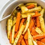 A bowl filled with roasted carrots and parsnips with a serving spoon in it.