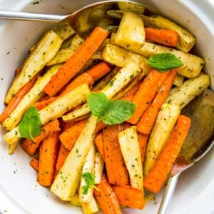 A bowl of roasted carrots and parsnips with serving spoons in it.