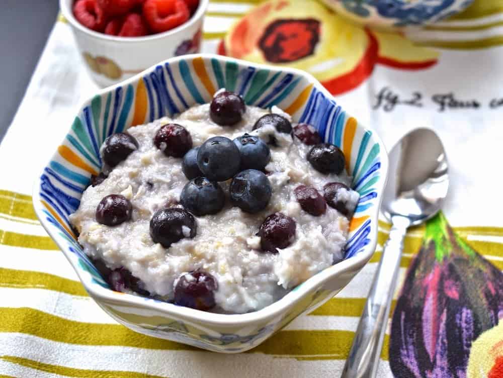 A bowl of paleo oatmeal topped with fresh blueberries and a spoon beside it.