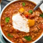 A bowl of chili topped with sour cream with a spoon in it.