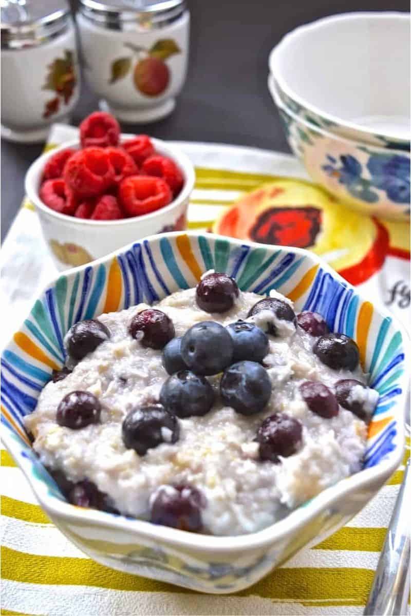 A bowl of oatmeal topped with fresh blueberries with a spoon next to it.