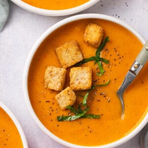 A bowl of butternut squash and red pepper soup topped with croutons.