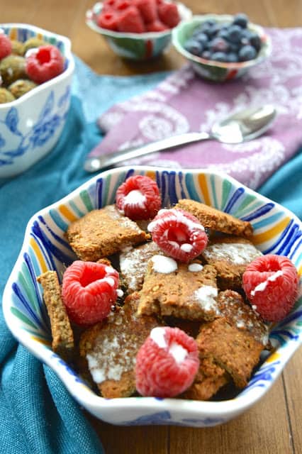 A bowl of cereal with milk and topped with raspberries. 