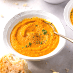 A bowl of creamy carrot turnip soup, garnished with fresh parsley.