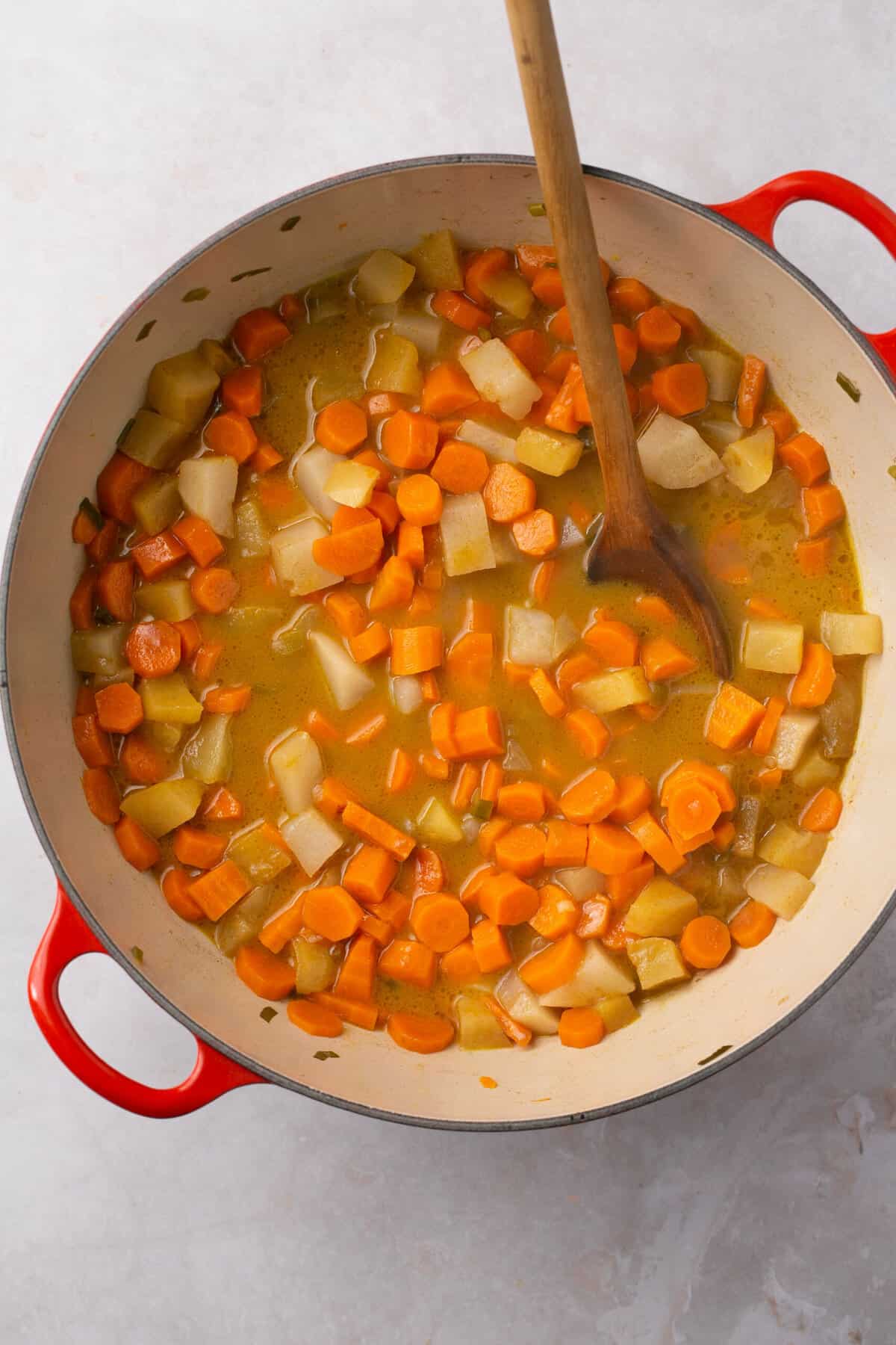 A pot with broth, chopped carrots, chopped turnips and a spoon in it.