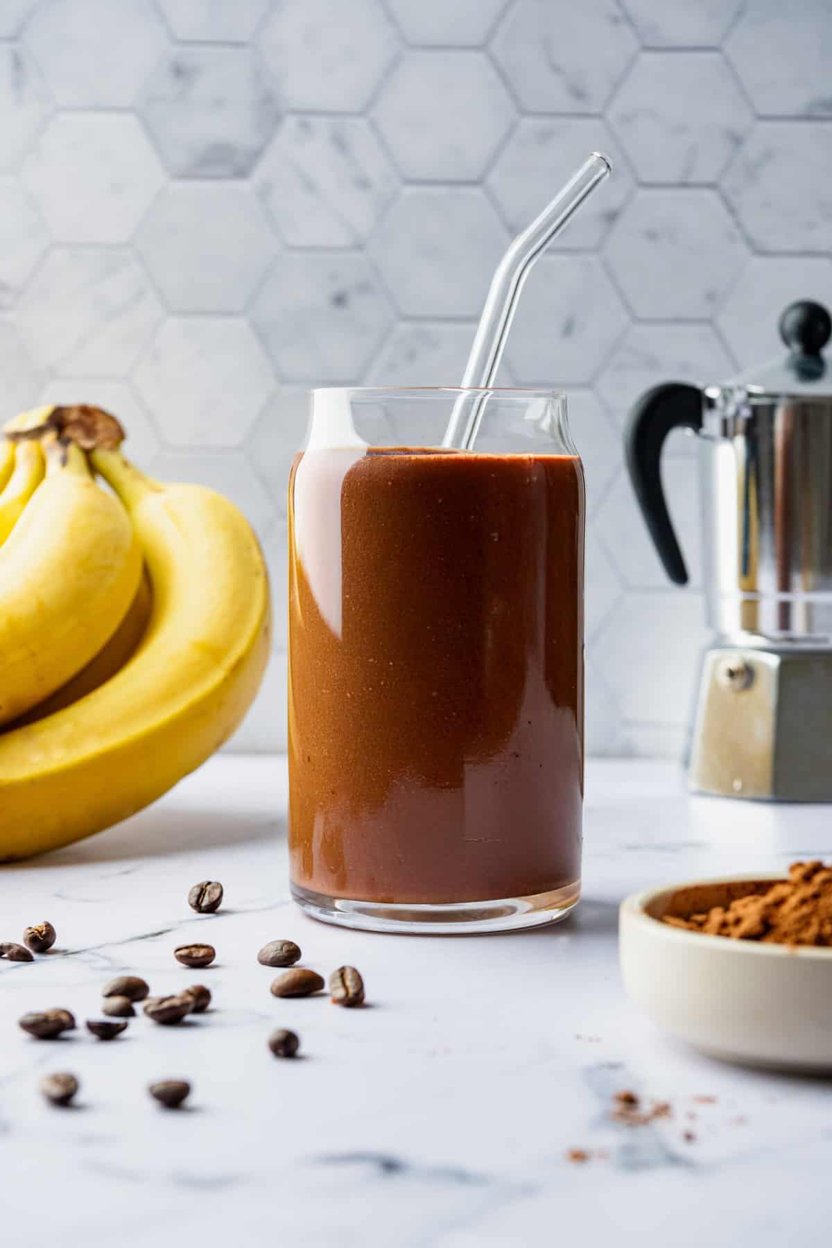 A chocolate smoothie in a glass with a glass straw in it.