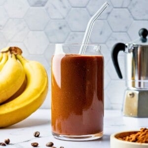 A glass filled with a chocolate smoothie with a glass straw in it.