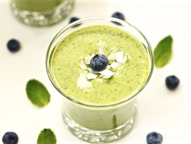 A glass filled with a peppermint smoothie, topped with fresh blueberries.