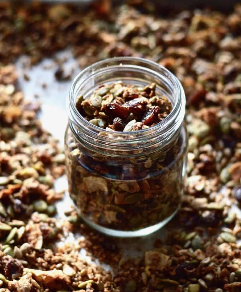 A jar of grain free granola on a baking sheet surrounded by more granola.