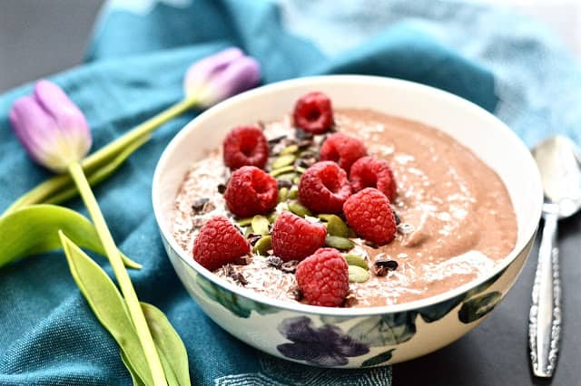 A chocolate raspberry smoothie bowl topped with shredded coconut, cacao nibs and fresh raspberries. 