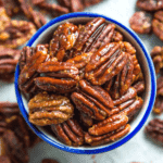 A bowl of honey glazed pecans, surrounded by more pecans.