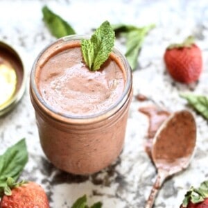A jar of strawberry basil vinaigrette topped with fresh mint leaves with a spoon beside it.