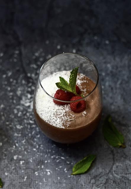 A glass filled with a chocolate mint smoothie garnished with shredded coconut and mint leaves. 