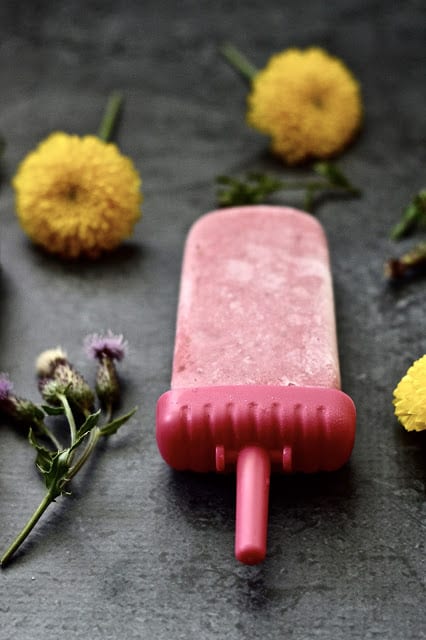 A raspberry popsicle surrounded by yellow flowers. 