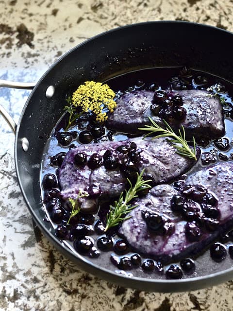 A pan filled with blueberry pork chops garnished with fresh rosemary. 