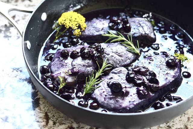 A pan filled with pork chops covered in blueberry sauce garnish with fresh rosemary. 