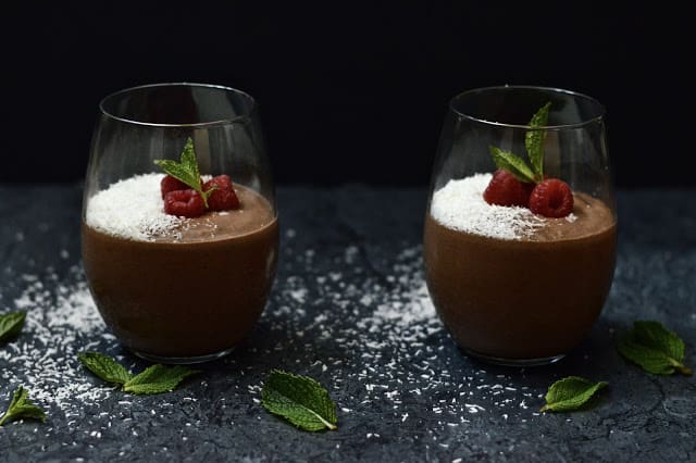 Two glasses filled with chocolate mint smoothie garnished with shredded coconut and mint leaves. 