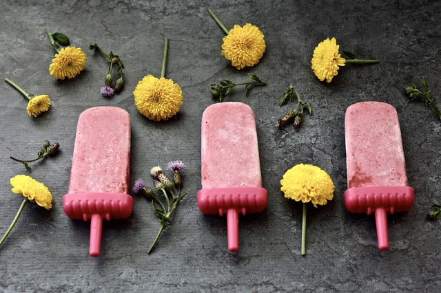 Three raspberries popsicles surrounded by yellow flowers. 