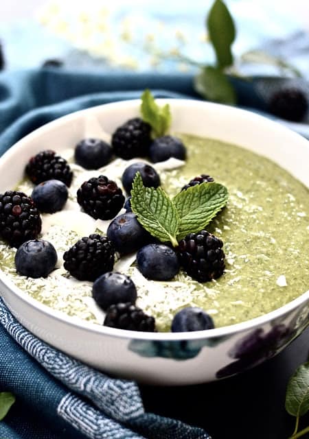 A mint smoothie bowl topped with blueberries, shredded coconut and blackberries