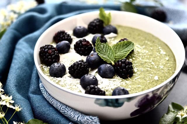 A mint smoothie bowl topped with shredded coconut, blueberries and cacao nibs.