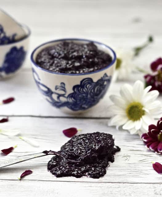 A spoon full of blueberry chia jam with fresh flowers around it.