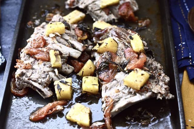 A tray of cooked pineapple pork ribs garnished with tomatoes and fresh herbs. 