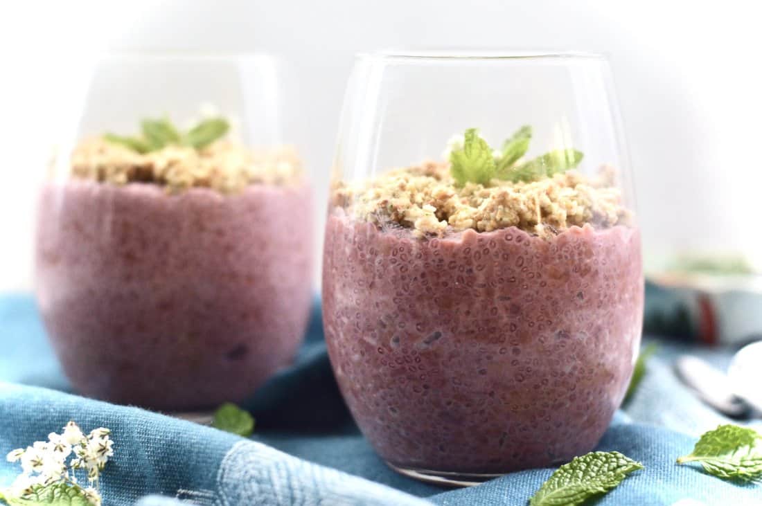 Two glasses filled with raspberry chia pudding topping with fresh mint leaves. 