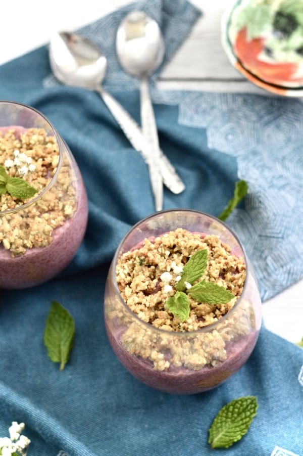 A glass filled with raspberry chia pudding with a cashew mint crumble topping on top.