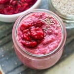 A jar of raspberry chia pudding topped with fresh raspberries and white chia seeds.