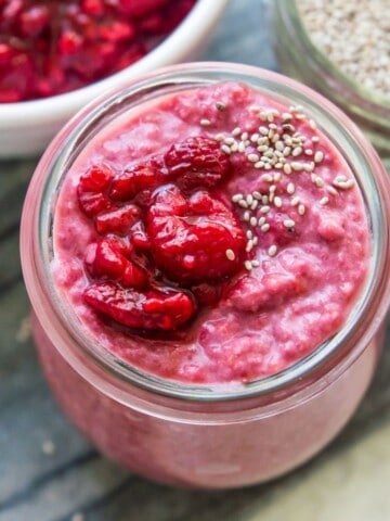 A jar of raspberry chia pudding topped with fresh raspberries and white chia seeds.