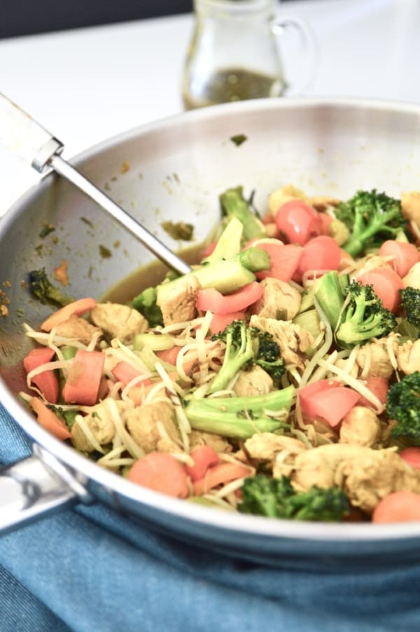 A stainless steel wok filled with an chicken vegetable stir fry with a serving spoon in it.