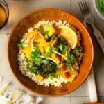 A bowl of orange ginger chicken stir fry over cauliflower rice with a fork next to the bowl.