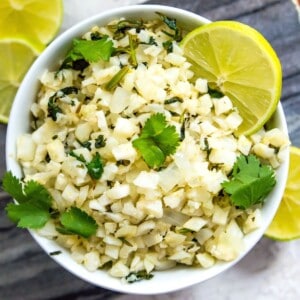 A bowl of cilantro lime cauliflower rice garnished with fresh cilantro and lime wedges.